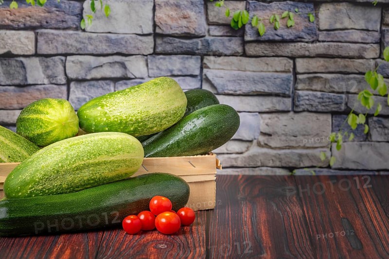 Courgettes (Cucurbita pepo), field cucumbers (Cucumis sativus), tomatoes (Solanum lycopersicum), on wood, in front of stone wall