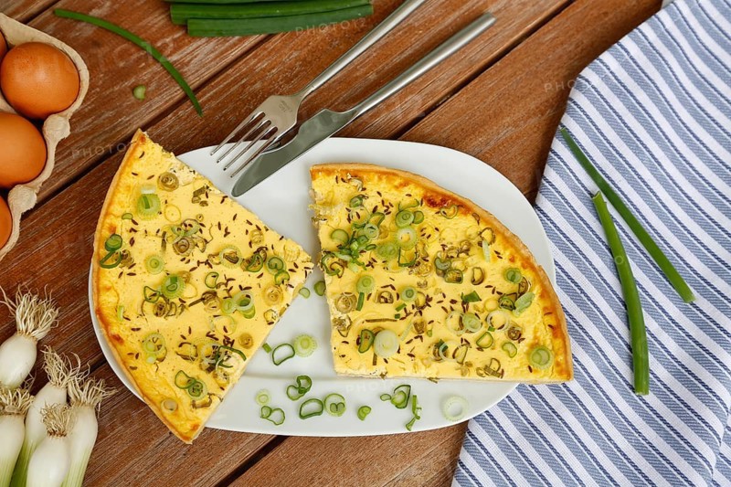 Swabian cuisine, salted cream cake with spring onions, hearty cake on serving platter, salty shortcrust pastry, baked, from the oven, baked goods, spring onions, winter onions, vegetarian, typical Swabian reinterpreted, baking, wooden stirring spoon, cooking spoon, wooden plate, eggs, fresh chicken eggs in egg carton, cutlery, knife, fork, wooden plate, traditional cuisine, food photography, studio, Germany, Europe