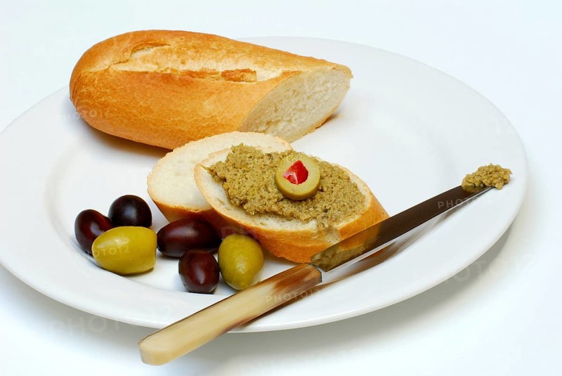 Tapenade on baguette, olives, olive paste, plate, knife, bread