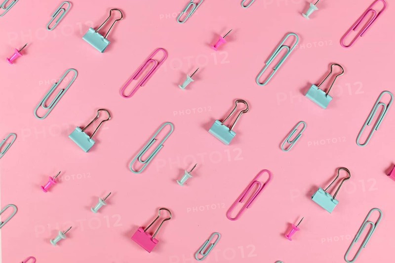 Stationery items like paper clips and drawing pins arranged on pink background