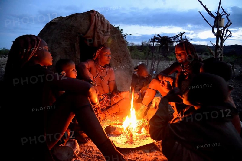 Himba women sitting around a fire in the early morning, Ombombo, Kaokoland, Kunene, Namibia, Africa