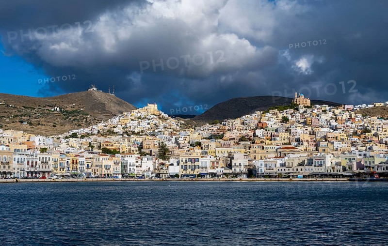 View of the town of Ermoupoli with pastel-coloured houses and sea, on the hill Anastasi Church or Church of the Resurrection and Basilica of San Giorgio in Ano Syros, dramatic cloudy sky, Ermoupoli, Syros, Cyclades, Greece, Europe