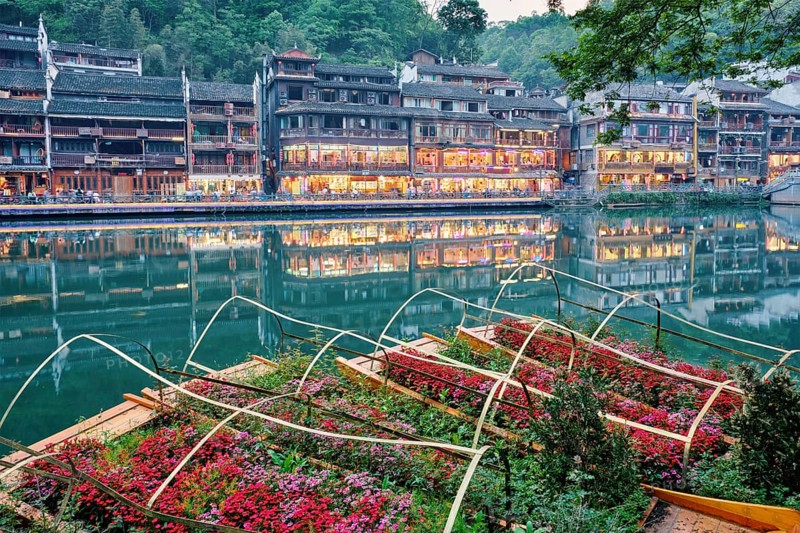 Chinese tourist attraction destination, Feng Huang Ancient Town (Phoenix Ancient Town) on Tuo Jiang River with flower beds on boats illuminated at night. Hunan Province, China, Asia