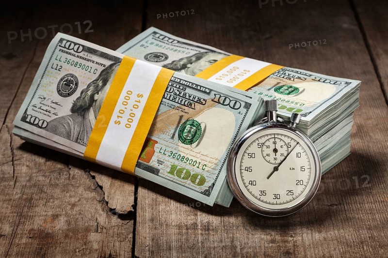 Time is money loan concept background, stopwatch and stack of new 100 US dollars 2013 edition banknotes bills bundles on wooden background
