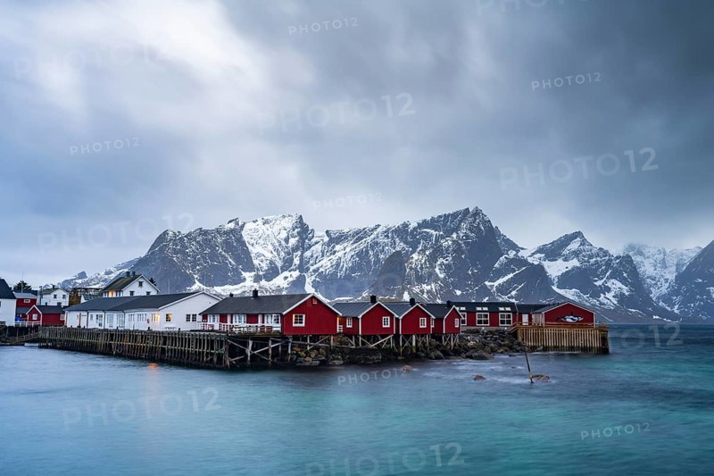 Rorbuer cabins of Hamnoy by the fjord, snowy mountains in the back, Hamnøy, Reine, Moskenesøya, Lofoten, Norway, Europe