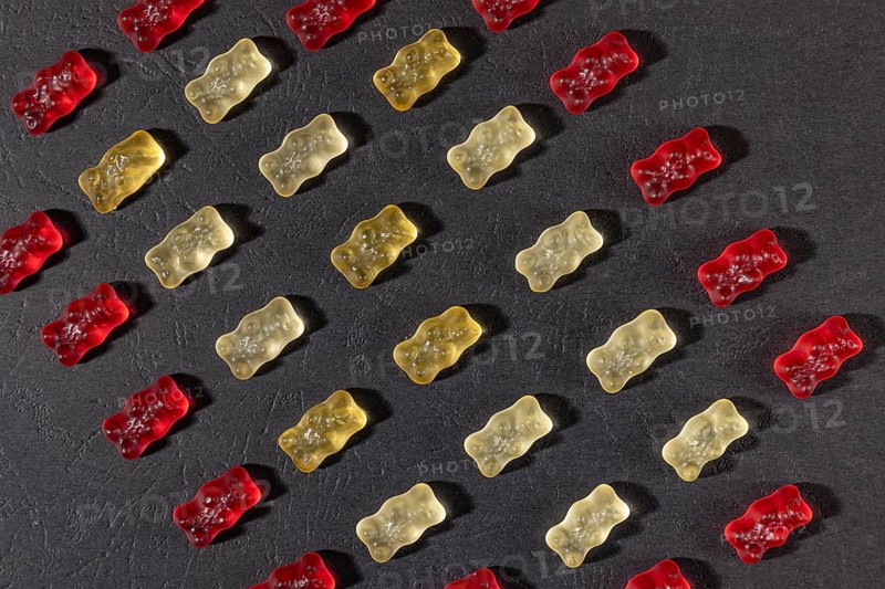 Different coloured gummy bears in rows, on a dark background