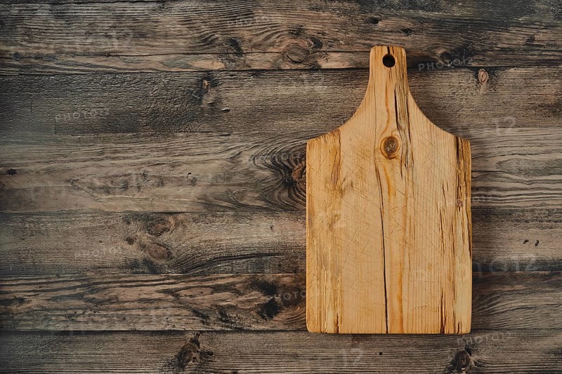 A wooden cutting board rests on a rustic wooden table, showcasing its natural grain and texture in a cozy kitchen environment illuminated by midday light