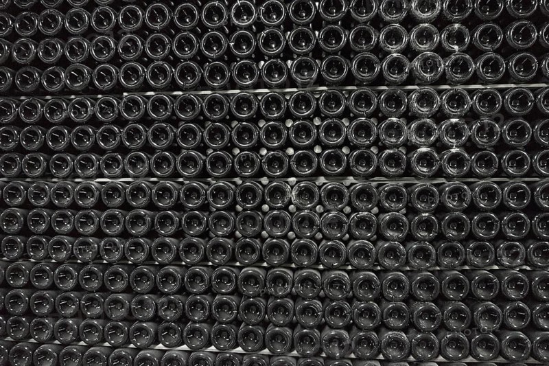 Sparkling wine is aged in bottles in a dark cellar background