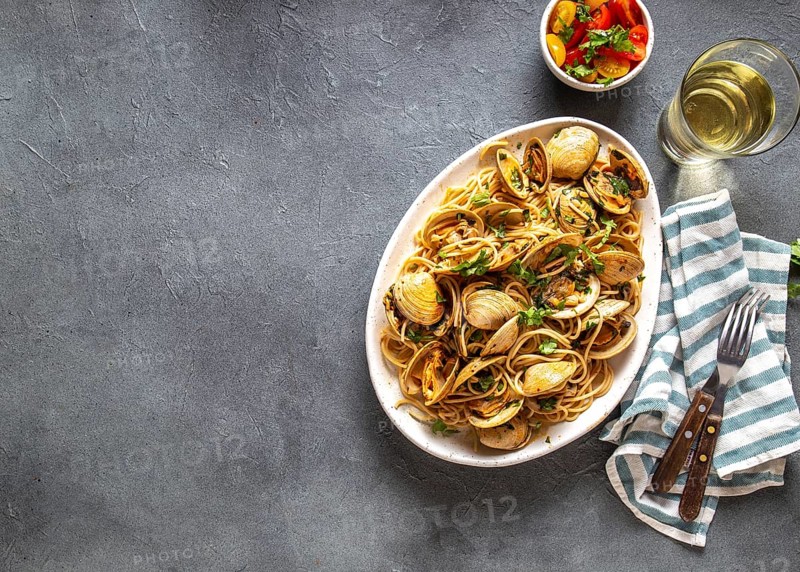 Seafood Pasta. ITALIAN SPAGHETTI ALLE VONGOLE. Clams spaghetti on white plate with white wine, gray background. Top view