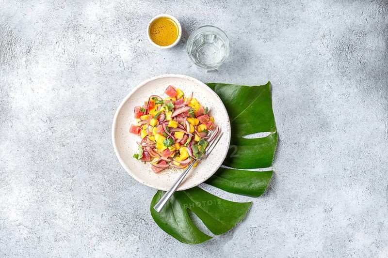 Tropical Hawaiian tahitian tuna mango salad on white plate on tropical monstera leafe