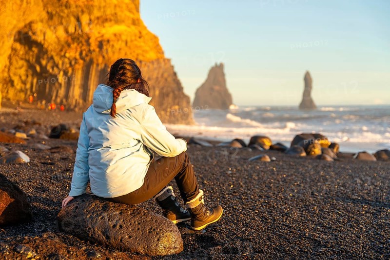 Female hiker sitting on the black sand beach of Reynisfjara looking at the sea. Iceland