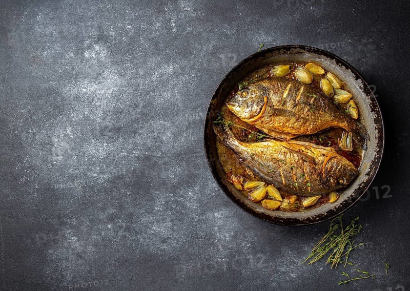Baked sea bream or dorada with onion and herbs in pan on dark background