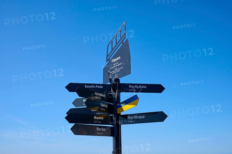 Black signpost against a blue sky with directions to various towns and destinations, Fløibanen mountain station, Bergen, Vestland, Norway, Europe