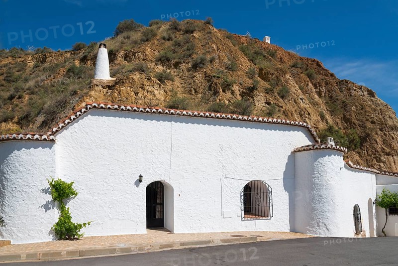 White-painted building with chimney and windows in front of a rock face, under a sunny blue sky, Pedro Antonio de Alarcon cave hotel, Guadix, Granada province, Andalusia, Spain, Europe