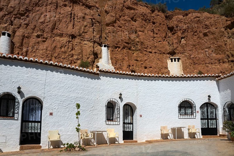 White building with arches and chairs in front of a rock face, under a sunny sky, Pedro Antonio de Alarcon cave hotel, Guadix, Granada province, Andalusia, Spain, Europe