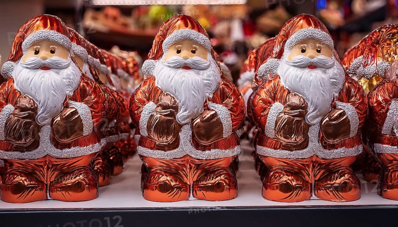 Symbol image for chocolate Santas wrapped in aluminium foil, cheerful looking Santas lined up on a shelf in a shop, AI-generated image, AI generated