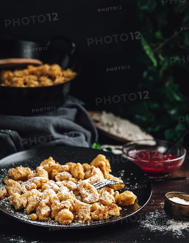 Kaiserschmarrn on a black plate sprinkled with sugar, pan in the background, dark surroundings