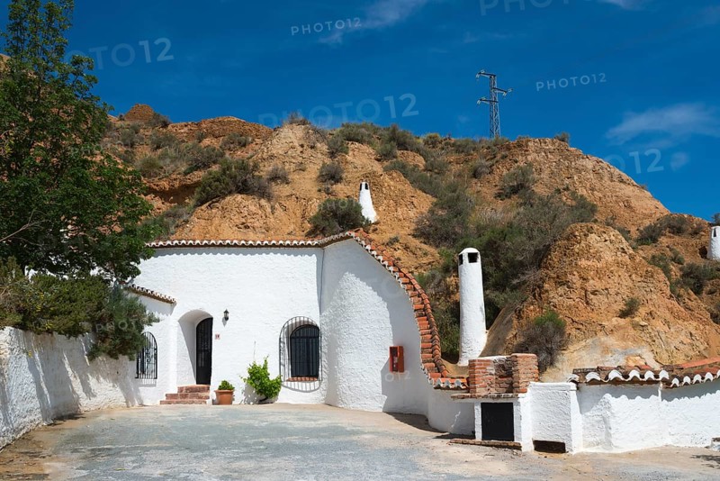 Small white building with chimney, tree and rock face in the background under a sunny blue sky, Pedro Antonio de Alarcon cave hotel, Guadix, Granada province, Andalusia, Spain, Europe