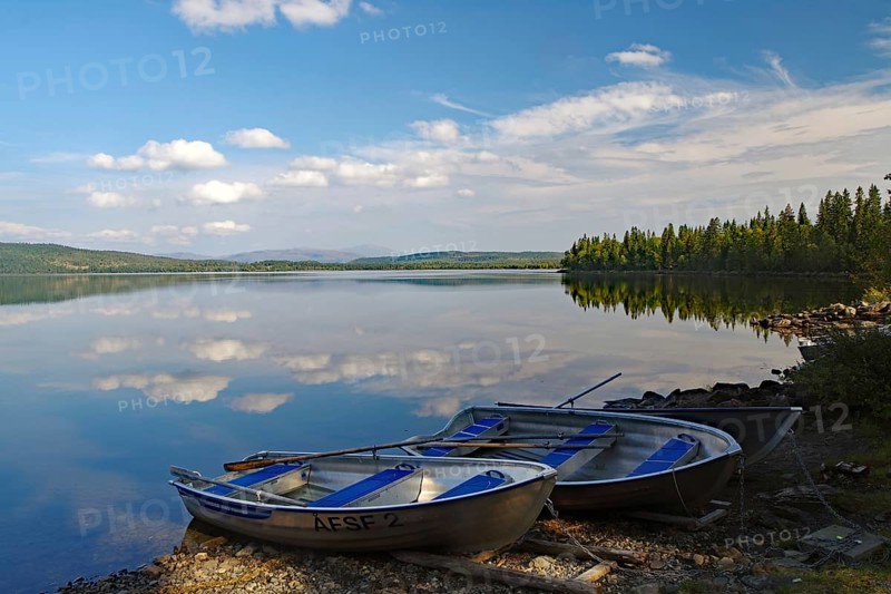 A calm lake with two docked boats, surrounded by trees and a slightly cloudy sky, Viken, Störlien, Jämtland, Sweden, Europe