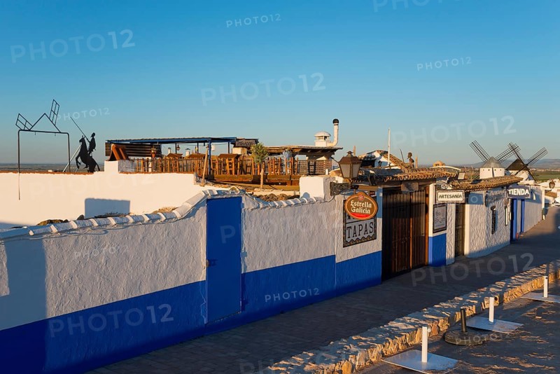 Rustic building with white and blue walls, tapas signs and windmills in the background under a bright sun, Campo de Criptana, Ciudad Real province, Castilla-La Mancha, Don Quixote Route, Spain, Europe