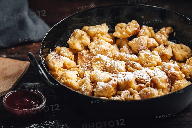 Kaiserschmarrn in a pan sprinkled with sugar, jam, dark background