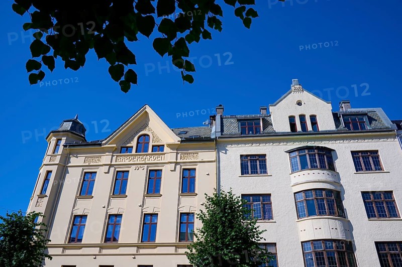 A historic building with an elaborate façade and many windows, surrounded by green trees under a clear blue sky, Bergen, Vestland, Norway, Europe
