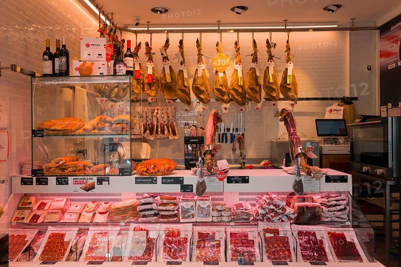Modern butcher's shop with meat counter, hanging hams, sausages and wine bottles on display, illuminated and neatly arranged, Nerja, Province of Málaga, Malaga, Costa del Sol, Andalusia, Spain, Europe