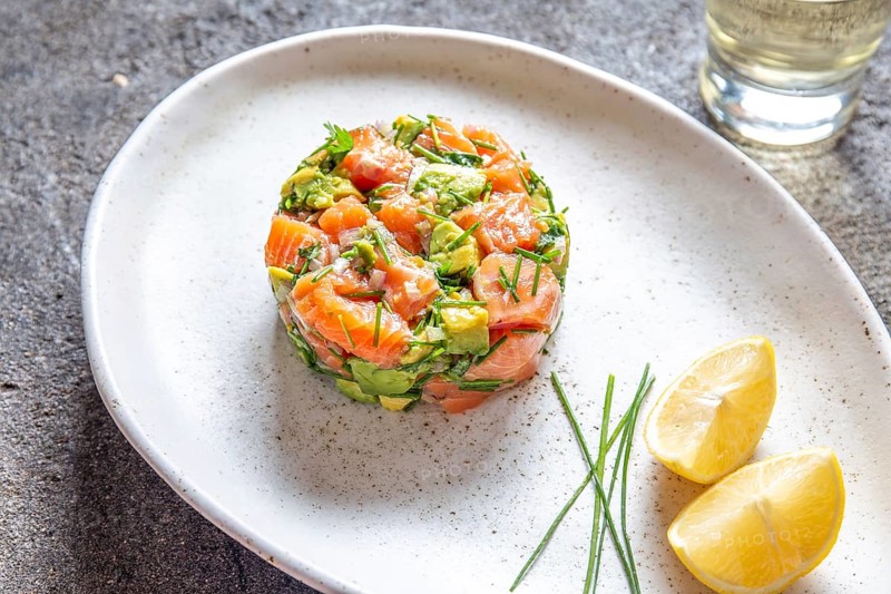 PERUVIAN FOOD. Salmon ceviche with avocado, spring onion and lemon on white plate served with white wine