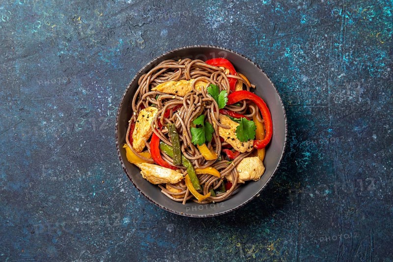 Japanese dish buckwheat soba noodles with chicken and vegetables carrot, bell pepper and green beans in grey bowl, top view, copy space