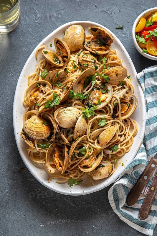 Seafood Pasta. ITALIAN SPAGHETTI ALLE VONGOLE. Clams spaghetti on white plate with white wine, gray background. Top view