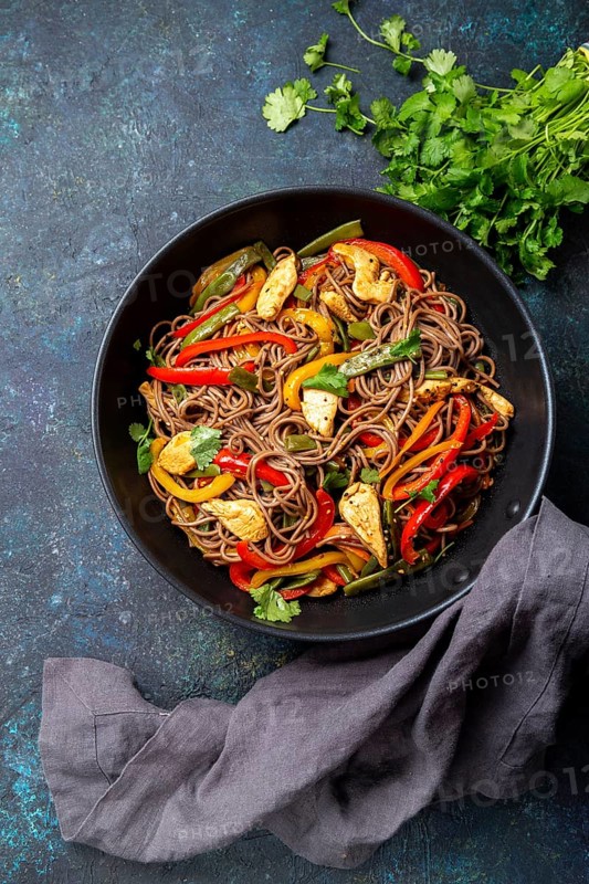 Japanese dish buckwheat soba noodles with chicken and vegetables carrot, bell pepper and green beans in wok on dark blue background