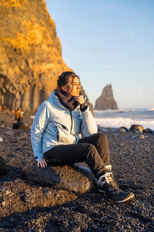 Portrait of a woman sitting on the black sand beach of Reynisfjara looking at the sea. Iceland