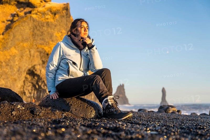 Portrait of pretty woman sitting on the black sand beach of Reynisfjara by the sea. Iceland