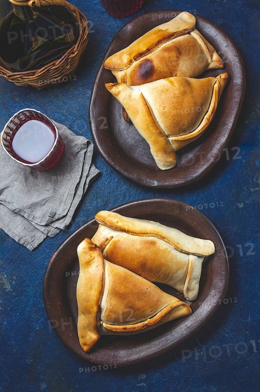 Food, Tipical Chilean baked empanadas de pino y napolitano on clay plates with wine. Dish and drink on 18 September party Independence day Chile, blue background
