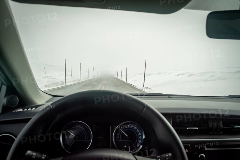 Car interior point of view on road cleared from snow and ice, but piled up on the side of the road. Winter driving