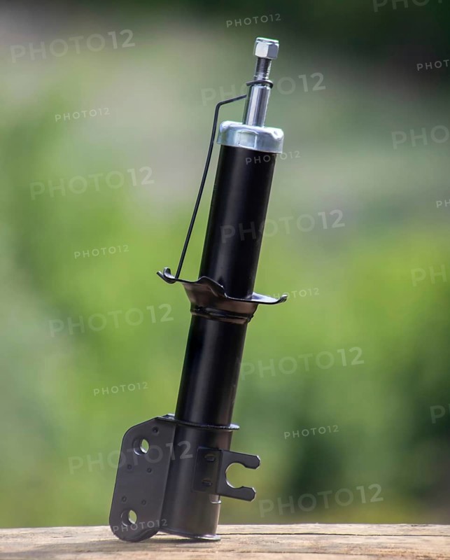 New shock absorber spare part car stands on a wooden board on a background of blurred green garden