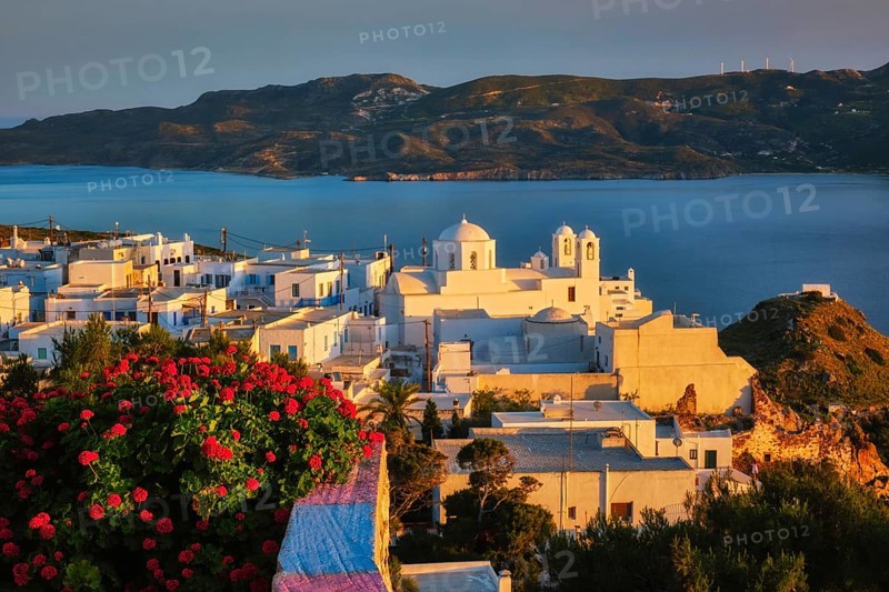 View of Plaka village on Milos island over red geranium flowers on sunset. Plaka town, Milos island, Greece, Europe