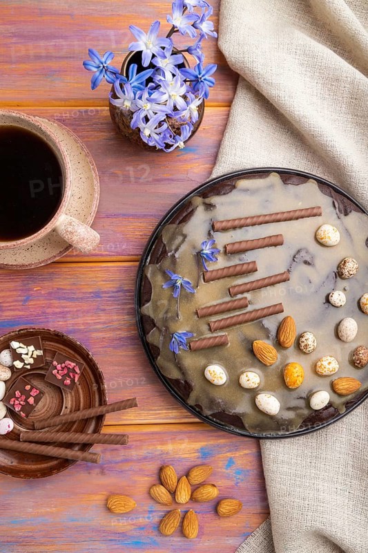 Homemade chocolate brownie cake with caramel cream and almonds with cup of coffee on a colored wooden background and linen textile. top view. flat lay, close up