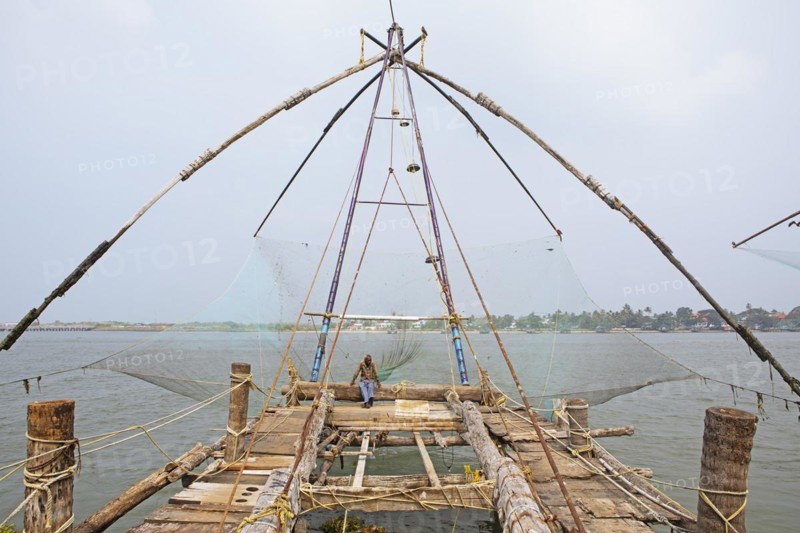 Indian fisherman sitting on a Chinese fishing net, behind him the Arabian Sea, Kochi, Kerala, India, Asia