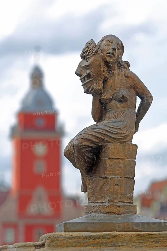 Sculpture Fides by Bernd Göbel 2021 with blurred Old Town Hall, historical, allegory, Roman, mythology, virtue, trust, loyalty, oath, faith, woman with large mask sitting on pedestal, depth of field, blur, horse trough, main market, Gotha, Thuringia, Germany, Europe