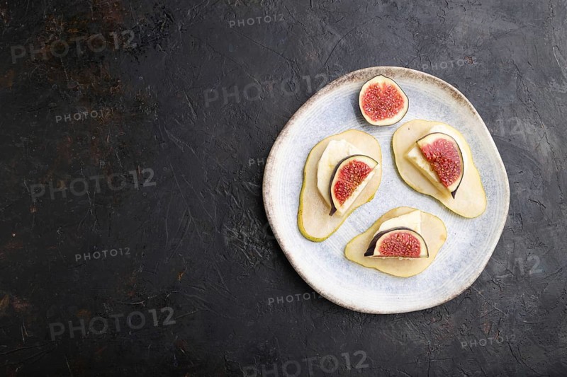 Summer appetizer with pear, cottage cheese, figs and honey on ceramic plate on a black concrete background. Top view, flat lay, copy space