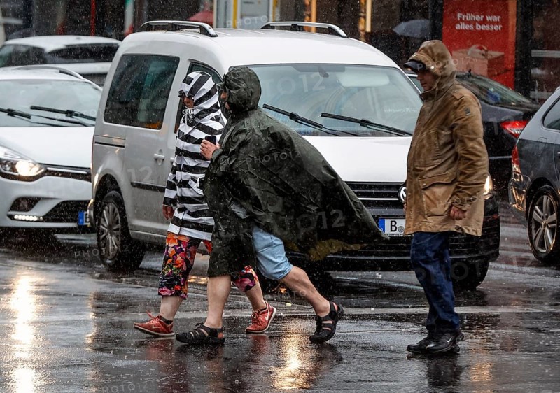 People in rain gear walking across a street in heavy rainfall, Berlin, 23 06 2023