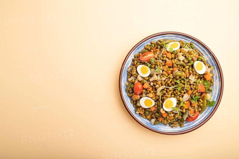 Mung bean porridge with quail eggs, tomatoes and microgreen sprouts on a pastel orange background. Top view, flat lay, copy space