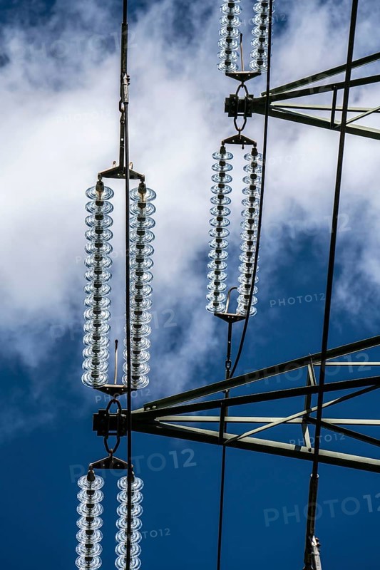 Insulators made of glass on a high-voltage line, they hang on the pylons as a suspension device between the pylon and the live, non-insulated cable, extra-high voltage line, symbolic image energy