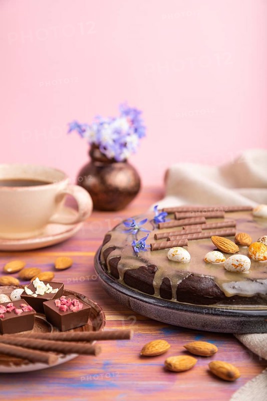 Homemade chocolate brownie cake with caramel cream and almonds with cup of coffee on a colored and pink background and linen textile. Side view, copy space, selective focus