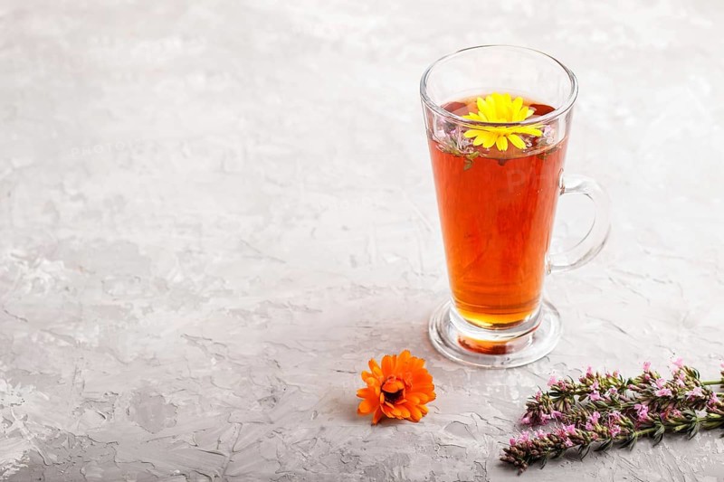 Glass of herbal tea with calendula and hyssop on a gray concrete background. Morninig, spring, healthy drink concept. Side view, selective focus, copy space