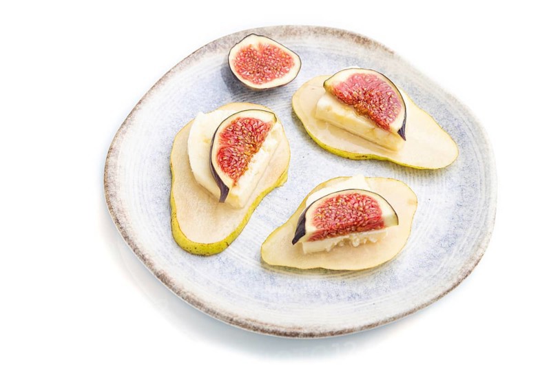 Summer appetizer with pear, cottage cheese, figs and honey on ceramic plate isolated on white background. Side view, close up