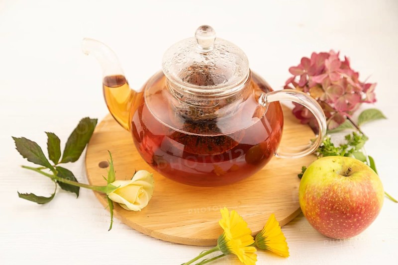 Red tea with herbs in glass teapot on white wooden background. Healthy drink concept. Top view, close up, selective focus