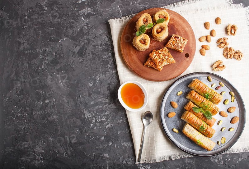 Set of various traditional arabic sweets: baklava, kunafa, basbus in ceramic plates on a black concrete background. top view, copy space