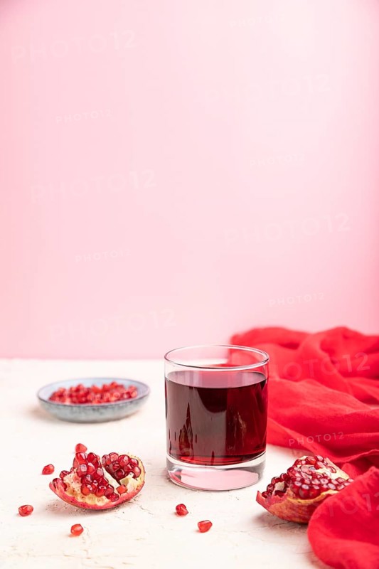 Glass of pomegranate juice on a white and pink background with red textile. Side view, copy space, selective focus